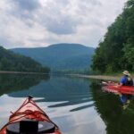 Man kayaks through trees, another kayak in the center